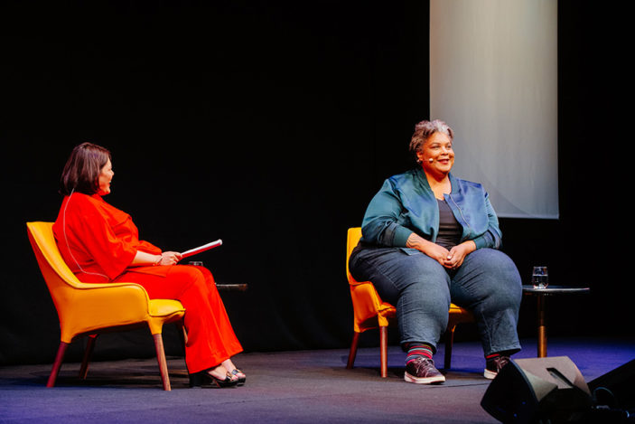 Two women sit on stage in conversation.