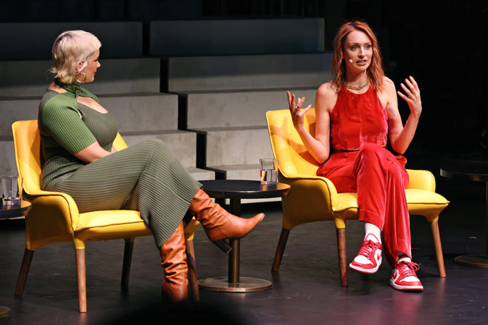 Two women speak together on stage.